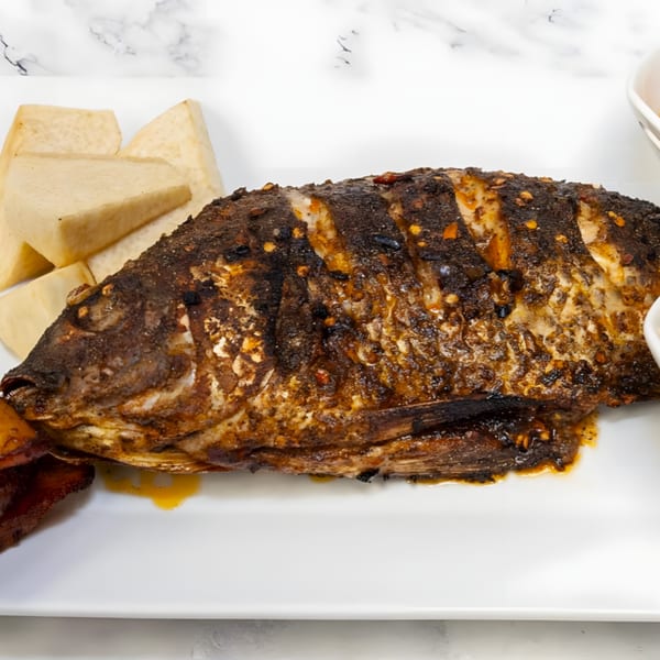 A whole grilled fish, seasoned and charred, served with white root vegetable wedges on a white plate.