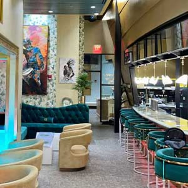 Aroma Restaurant & Lounge interior with a teal velvet couch, beige chairs, and a long bar with teal stools.