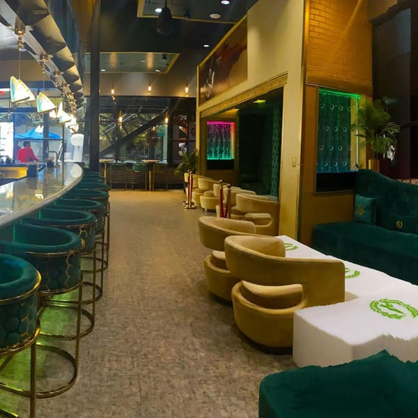 Aroma Restaurant & Lounge interior with a long bar, green bar stools, and yellow lounge seating.