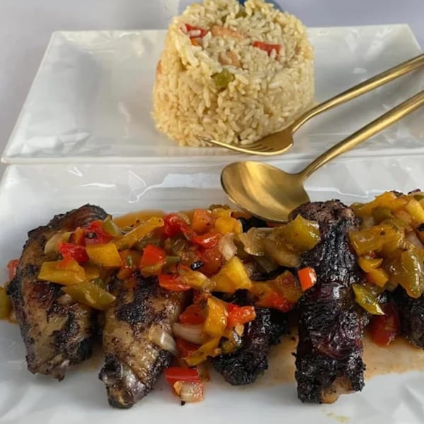 Grilled chicken wings topped with colorful bell peppers and onions, served with a side of rice.