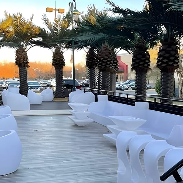 Outdoor patio at Aroma Restaurant & Lounge with white modern seating and palm trees.