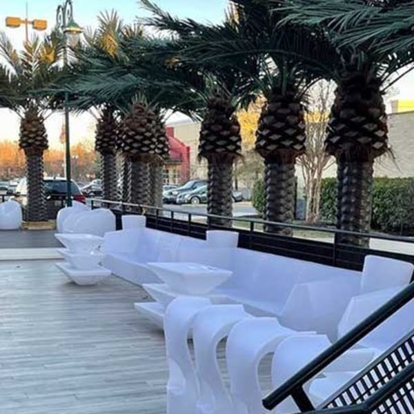 Outdoor patio with modern white seating, tables, and palm trees at Aroma Restaurant & Lounge.