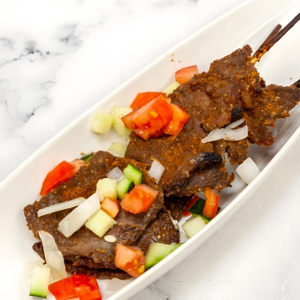 African-style beef skewers, seasoned and garnished with diced tomatoes, cucumbers, and onions.