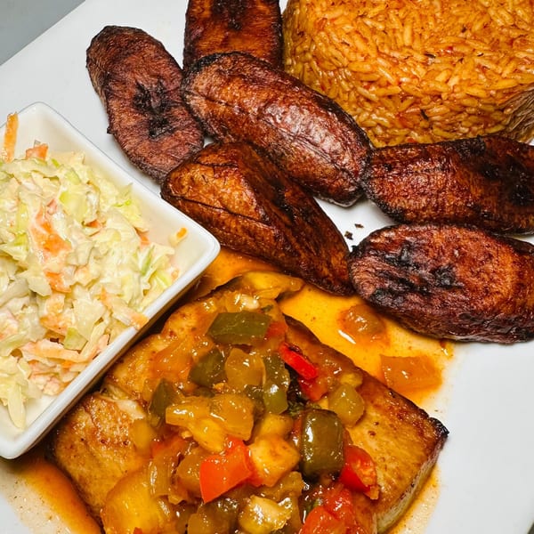 African meal with grilled fish, jollof rice, fried plantains, and coleslaw on a white plate.