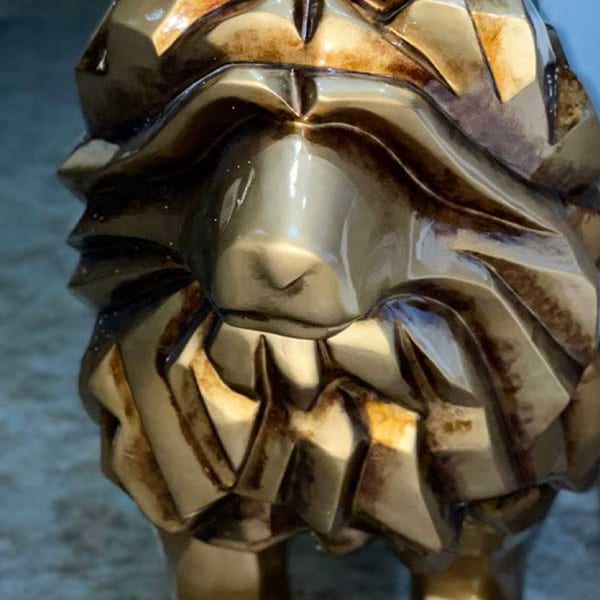 Close-up of a golden, geometric lion sculpture, showcasing its textured mane and snout.