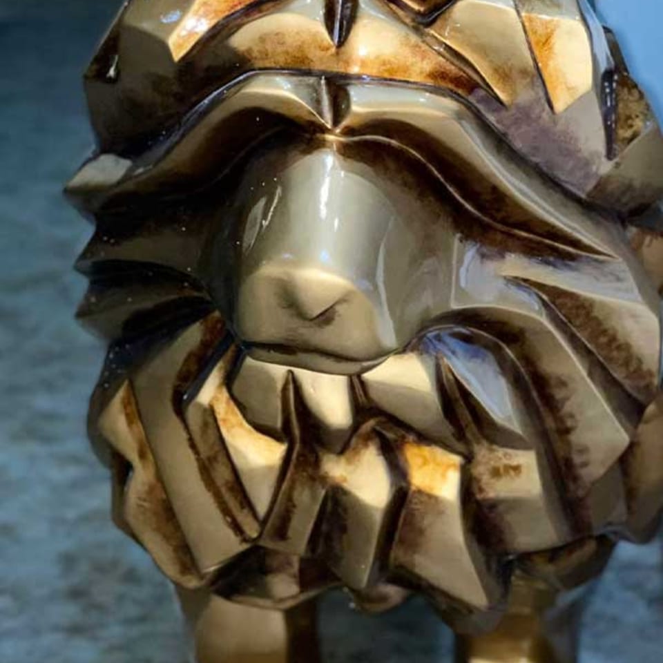 Close-up of a golden, geometric lion sculpture, showcasing its textured mane and snout.