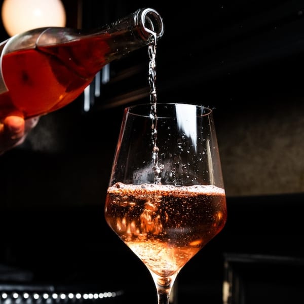 Rosé wine pouring from a bottle into a wine glass, creating bubbles.
